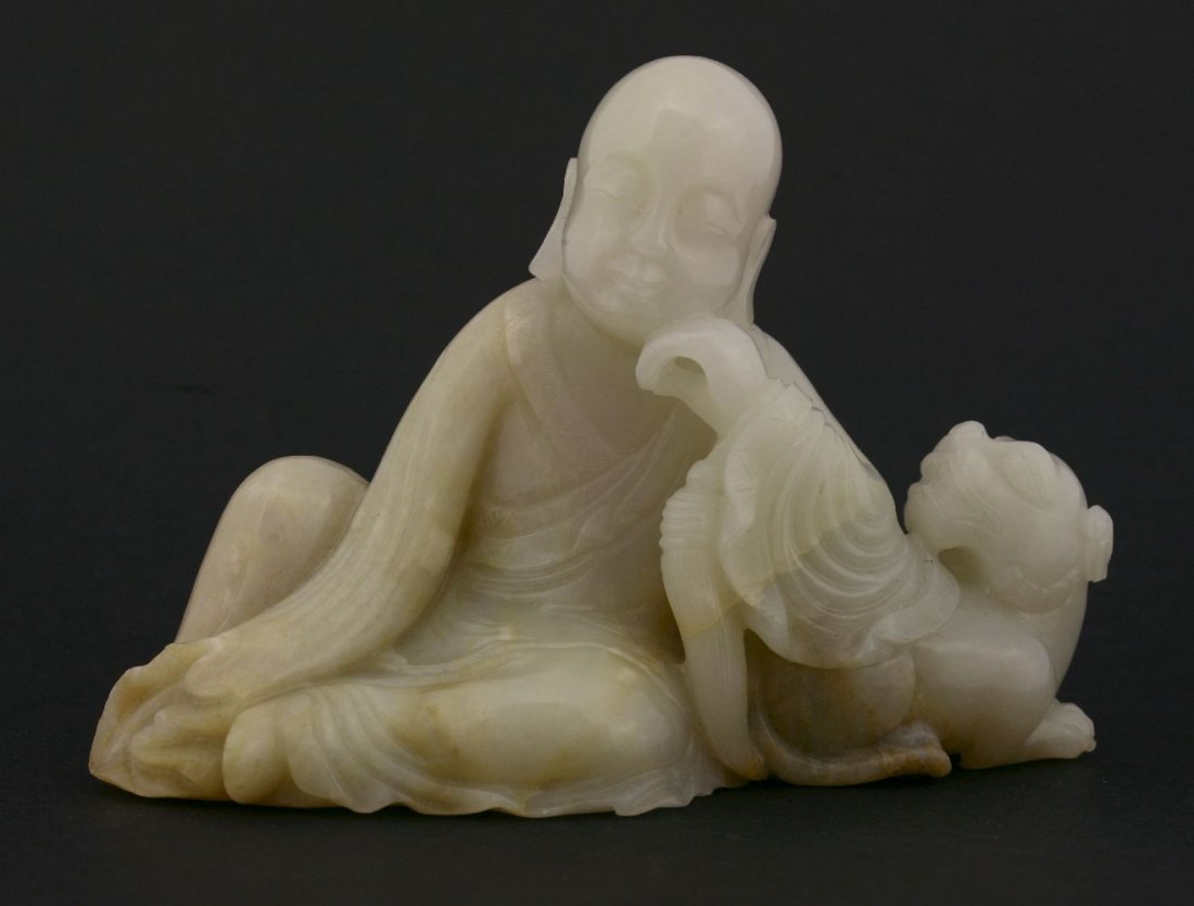 A jade Immortal, 19th century, resting in loose robes,: A jade Immortal, 19th century, resting in loose robes, on the back of a Buddhist lion, the stone ranging from white through grey-green to toffee,12.3cm