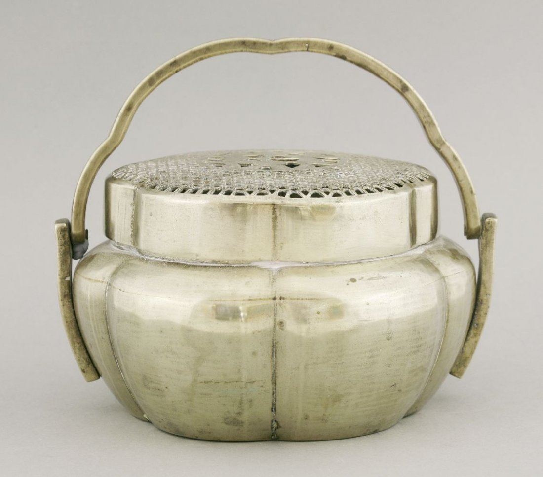 A polished brass Charcoal Heater, AFCearly 20th: A polished brass Charcoal Heater, AFCearly 20th century, the hexafoil cover pierced with florets around a central medallion of peaches and leaves, the lobed body conforming and with swing handle, 17cm