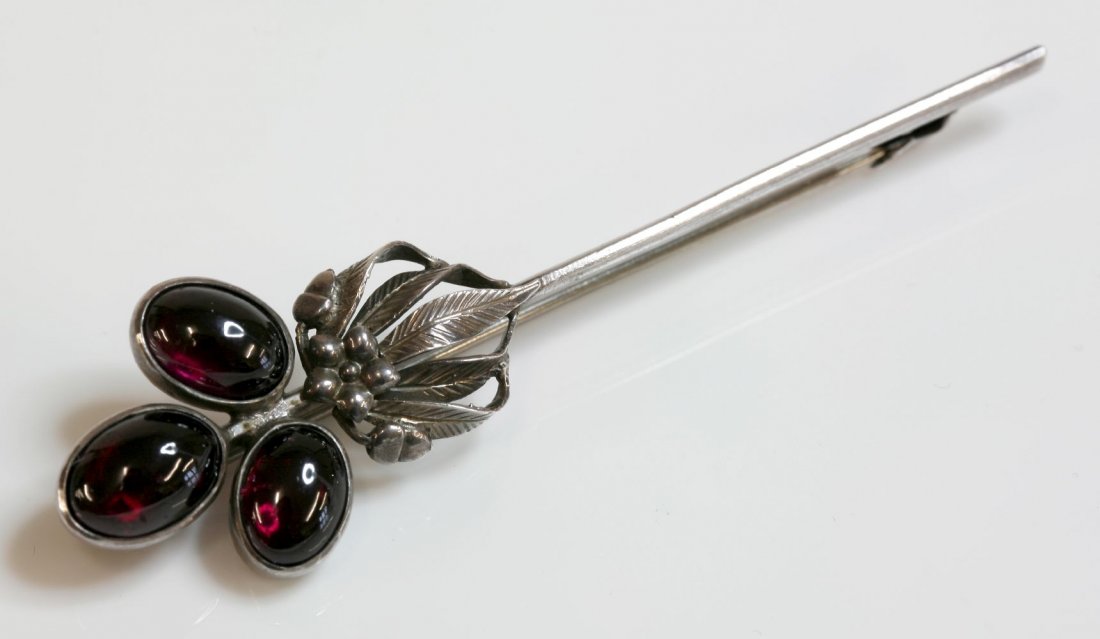 A silver Arts and Crafts garnet bar brooch, attributed: A silver Arts and Crafts garnet bar brooch, attributed to Bernard Instone, a trefoil cluster of three, oval cabochon garnets, rub set in plain collets to one end of the bar, with a spray of incised le