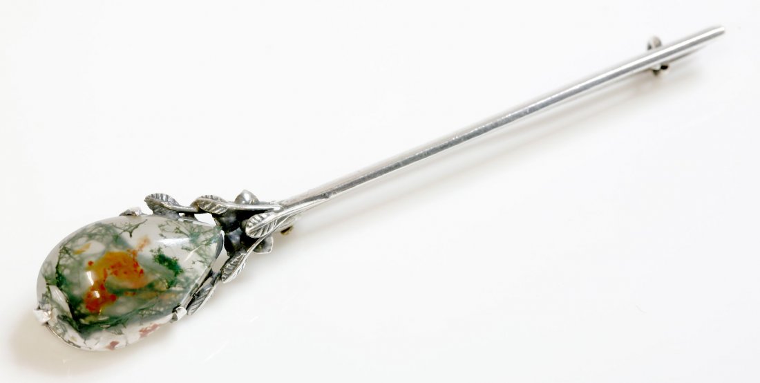 A sterling silver moss agate bar brooch, attributed to: A sterling silver moss agate bar brooch, attributed to Bernard Instone. The brooch 75mm long, with a pear shaped moss agate cabochon, three claw set to one end. A cluster of leaves and a flower head b