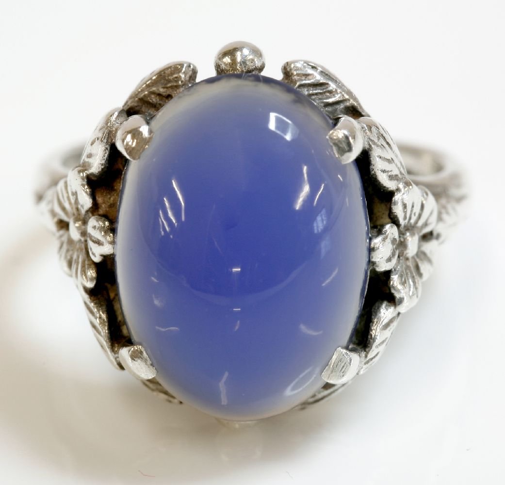 An Arts and Crafts silver single stone chalcedony ring,: An Arts and Crafts silver single stone chalcedony ring, attributed to Bernard Instone, an oval cabochon stained chalcedony, four claw set to the centre, with entwined, incised leaf shoulders, flower h