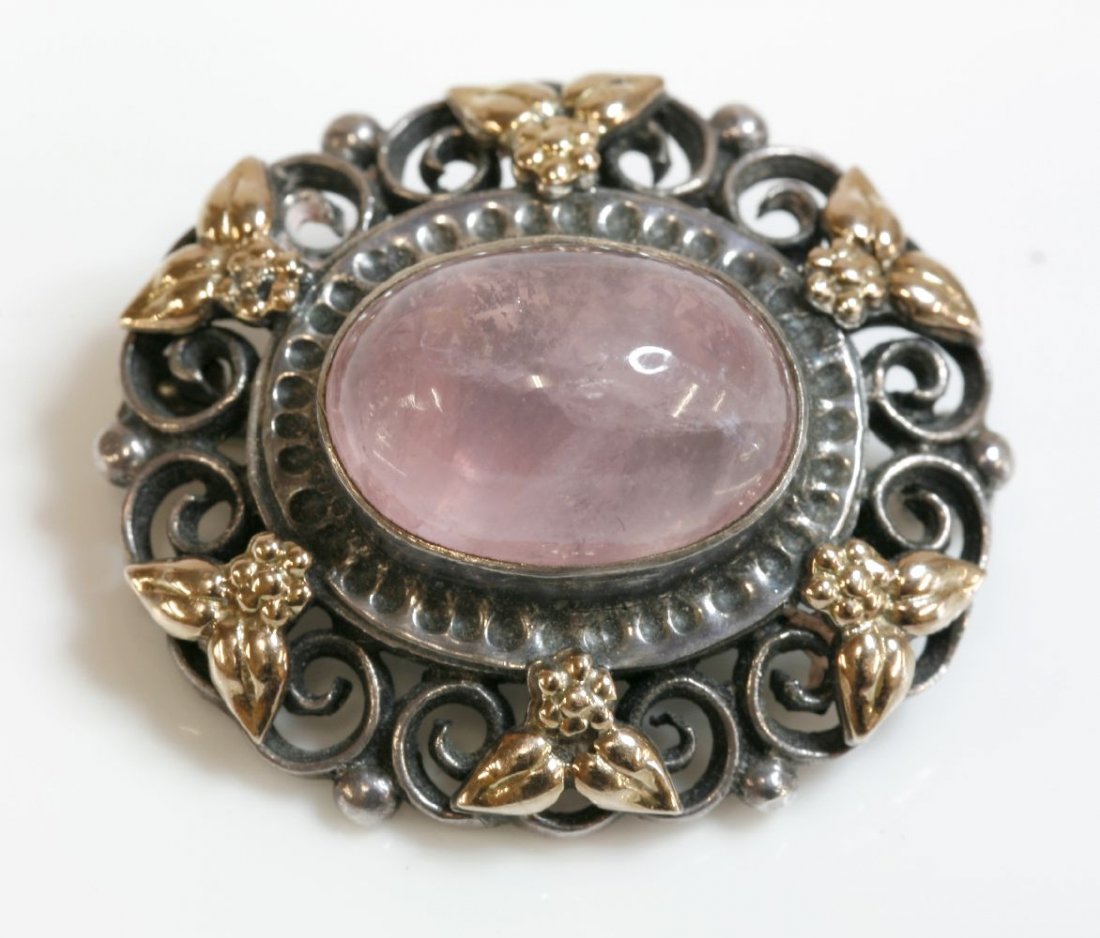 An Arts and Crafts silver and gold, rose quartz brooch,: An Arts and Crafts silver and gold, rose quartz brooch, attributed to Bernard Instone, an oval rose quartz cabochon rub set to the centre, with an indented surround, to an open 'C' scroll and bead bor