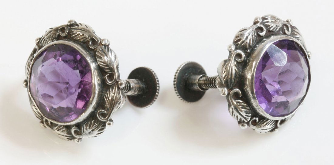 A pair of silver Arts and Crafts amethyst earrings,: A pair of silver Arts and Crafts amethyst earrings, attributed to Bernard Instone, a circular mixed cut amethyst rub set to a plain collet, with a leaf, vine and bead surround. Screw fittings. Marked