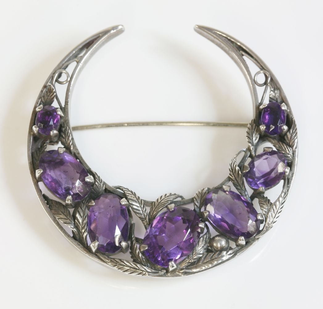 A silver Arts and Crafts amethyst crescent brooch,: A silver Arts and Crafts amethyst crescent brooch, attributed to Bernard Instone, a graduated crescent, 45mm diameter, with a flat wire frame and seven graduated oval mixed cut amethysts, four claw se