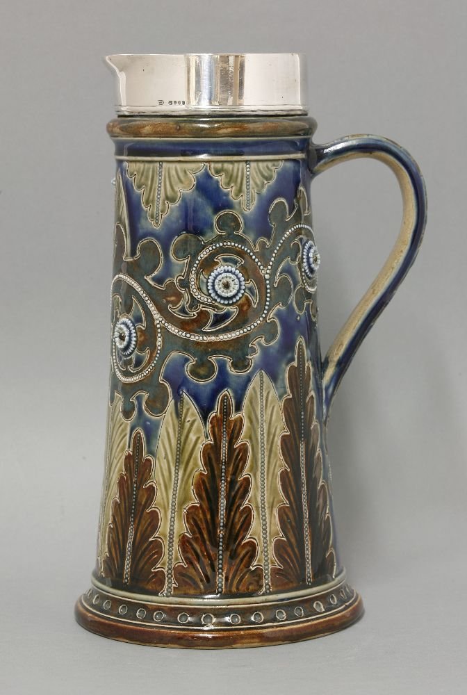 A Doulton Lambeth stoneware ewer, dated 1875, decorated: A Doulton Lambeth stoneware ewer, dated 1875, decorated by George Tinworth, the tapering body incised with scrolling foliage and leaves, with a silver collar by Thomas Johnson, London 1874, impressed