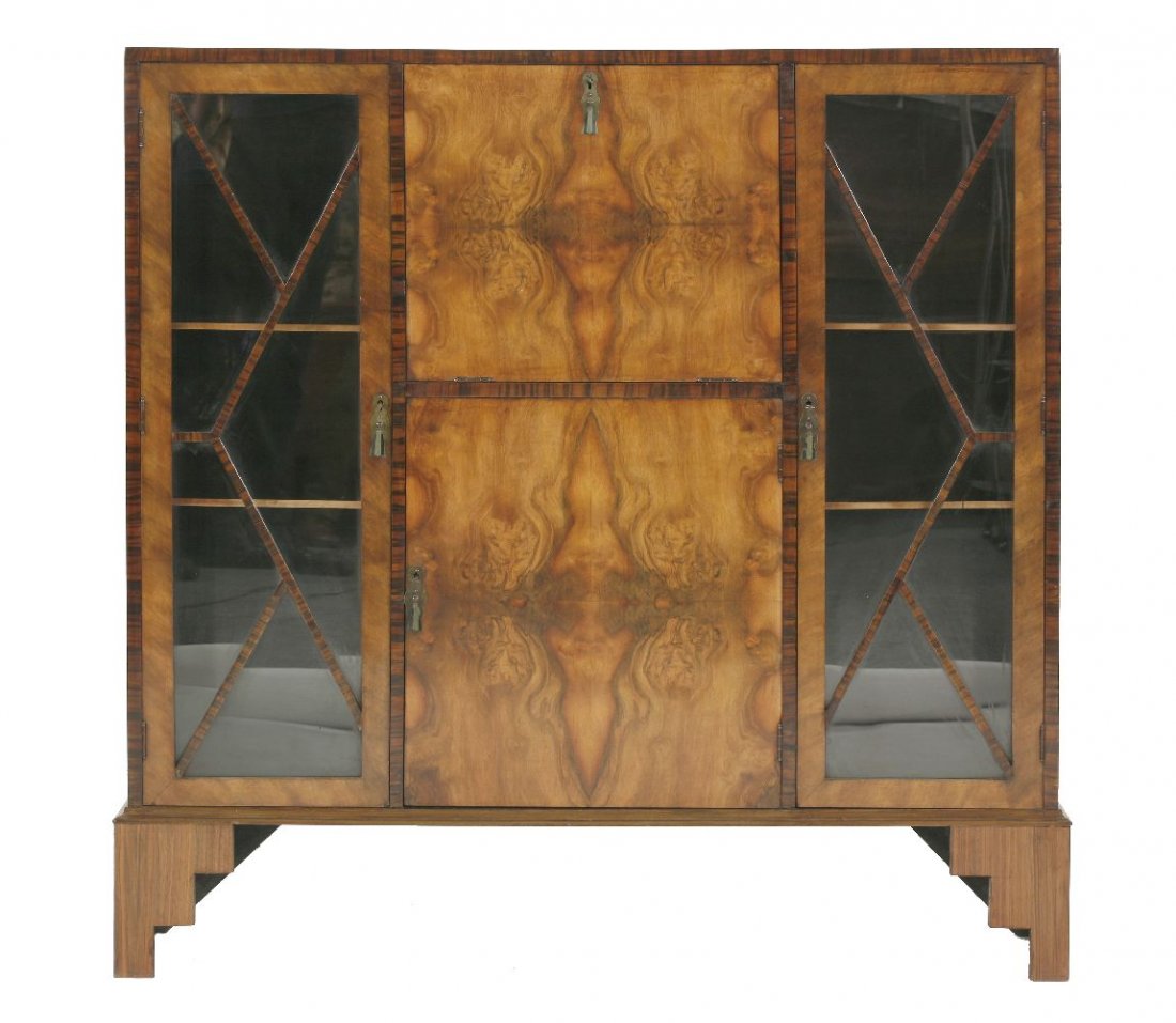An Art Deco walnut and coromandel bureau display: An Art Deco walnut and coromandel bureau display cabinet, the central hinged writing surface with pigeonholes and a pair of glass inkwells, over a cupboard flanked with glazed cupboards, on stepped br