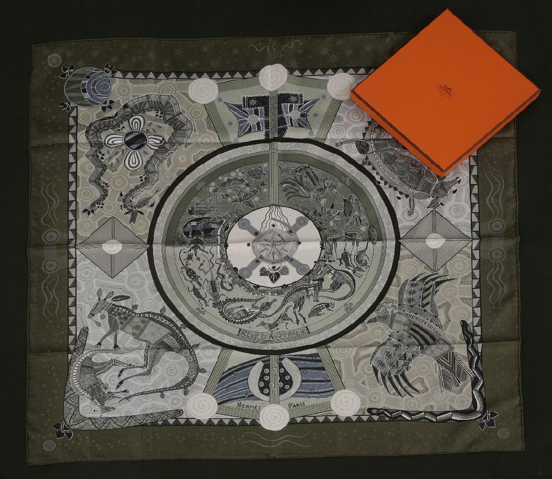 An Hermès silk scarf: An Hermès silk scarf, 'Reve Australie', designed by Zoe Pauwels, dark khaki green ground with printed Aboriginal design, in box with carrier bag