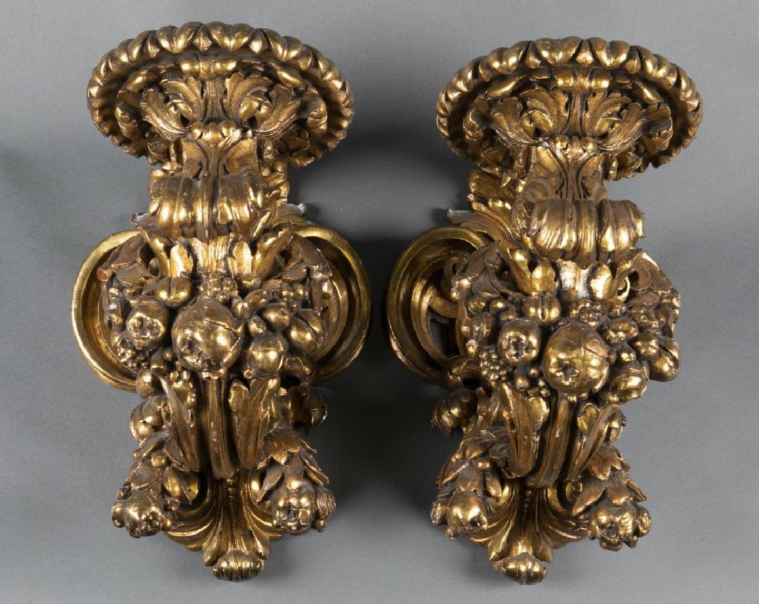 Pair of Baroque style gilt gessoed wall sconces.: A pair of two Baroque style gilt gessoed wall pricket sconces. Late 19th century. Floral and fruit festoon capped upward scroll arms cresting in foliate drop pans, supported by an openwork C-scroll sh