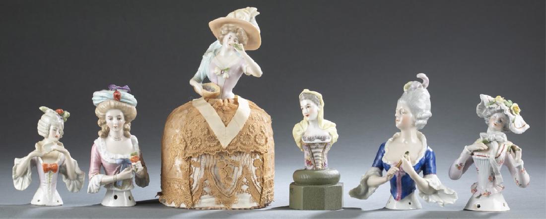 6 porcelain figural half dolls/pin cushions.: A group of six porcelain figural half dolls/pin cushions. ++ Woman porcelain pin cushion. 19th/20th century. Woman wears yellow shawl with flowers on bodice, on a plinth. Unmarked. 3 1/2". ++ Goebel f