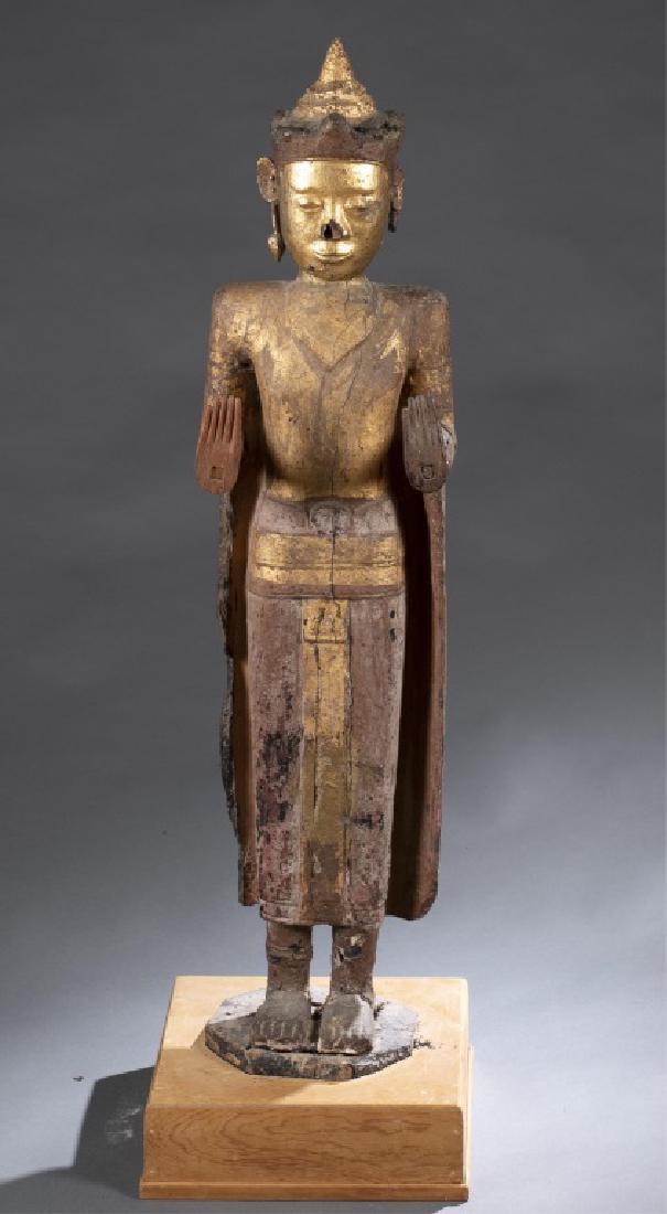 Gilt Cambodian Buddha w/base.: A gilt Cambodian Buddha with base. Wooden Buddha with red and gold lacquer, on custom made base. Standing Buddha in the gesture of calming the ocean, with both hands raised in Abhaya Mudra. One arm be