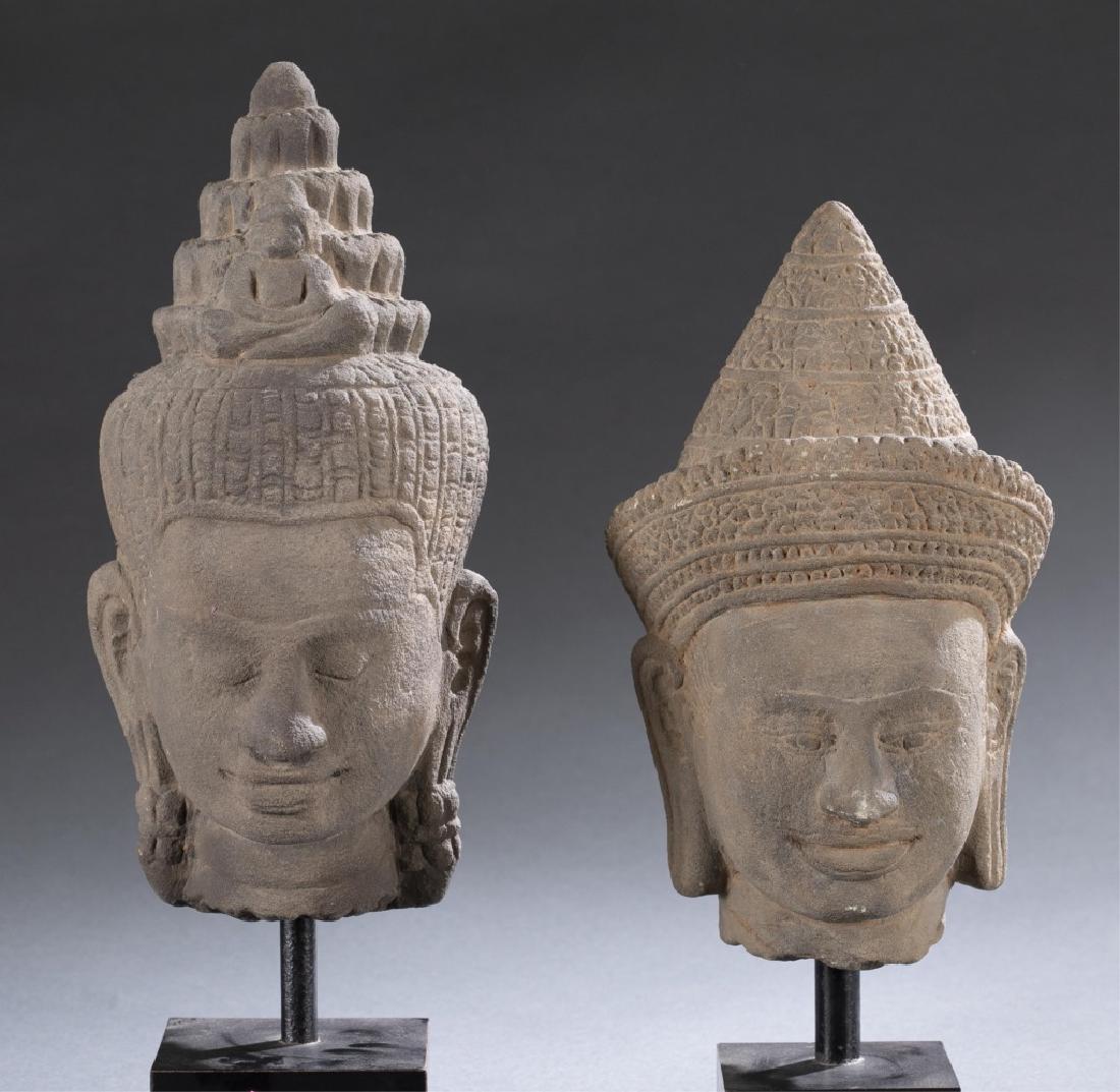 2 Cambodian stone Buddha heads.: A group of two Cambodian stone Buddha heads on stands. Sandstone Buddha head with pointed headdress on metal mounted square wood stands. Larger: 10 1/2"; 13 3/4"(w/stand). Smaller: 9 1/2"; 11 3/4"(w/s