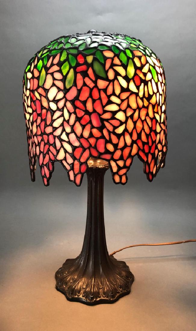 Tiffany style, Wisteria lamp, 20th century.: A Tiffany style pink wisteria lamp. 20th century. Reticulated top with wisteria pattern in pink and green leaded glass. Bronze base covered in oak leaf pattern with pillar-like stem. Overall: 19 1/2" 