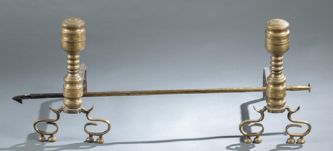 American brass andirons and fire poker, 1830.: A pair of American brass andirons and fire poker. Circa 1830. ++ Ring-turned shaft and cup finial with flattened top, raised on spurred, scrolled supports on flattened ball feet. 17" x 17" x 9 1/2". +