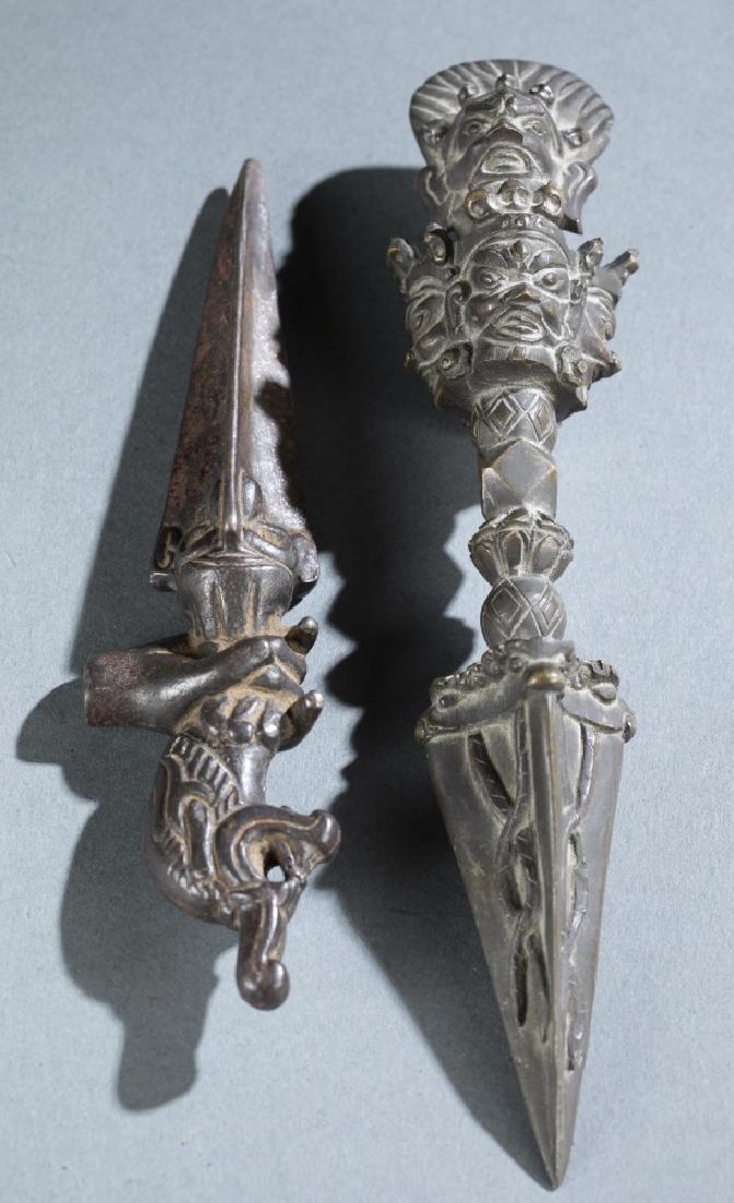 2 Tibetan Buddhist Kila/ Phurba implements.: A group of two Tibetan Buddhist Kila/ Phurba implements. Copper alloy. ++ Handle depicting multiple-headed guardian. With incised twisted decorations on the tip. 9 1/2" x 2 1/4". ++ Handle with a hand