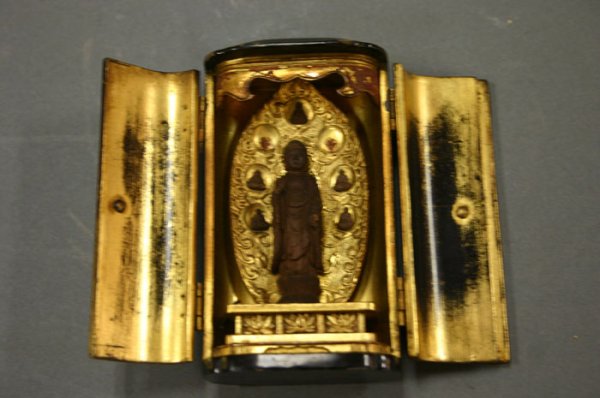 Small carved wood Buddah shrine statue in: Small carved wood Buddah shrine statue in a gilt & black enamel box with metal hardware. 4 1/2"h x 2 1/2"w (closed) x 1 1/2"d