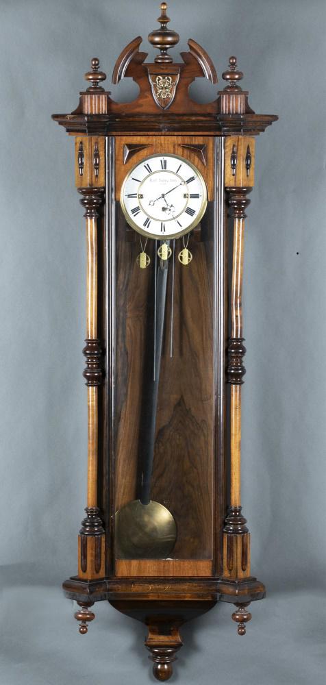 Carl Suchy & SÃ¶hne, regulator wall clock.: A Carl Suchy & SÃ¶hne regulator wall clock. Austrian. 20th century. Wooden case with decorative architectural and mask carving. Painted dial with Roman numerals. Includes three weights and pendulum.