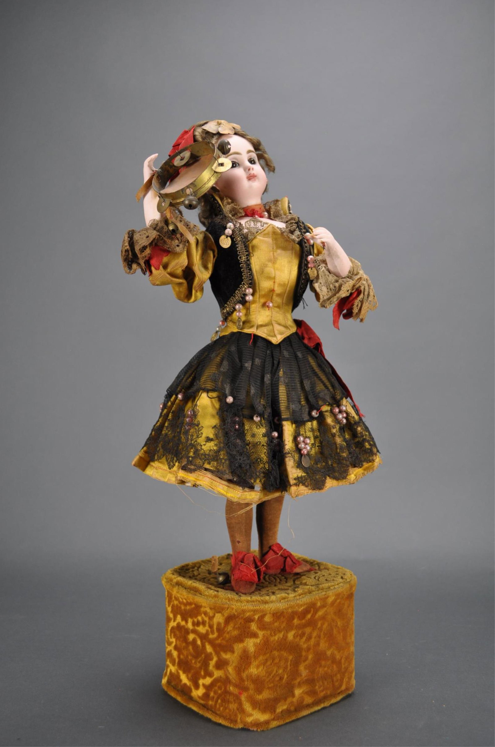 Automaton. Girl Playing Tambourine. Lambert.: 20" (51 cm.) Standing upon a velvet-covered base is a bisque swivel-head doll with bisque shoulder plate, blue glass paperweight eyes, dark eyeliner, painted lashes, shaded nostrils, closed mouth with
