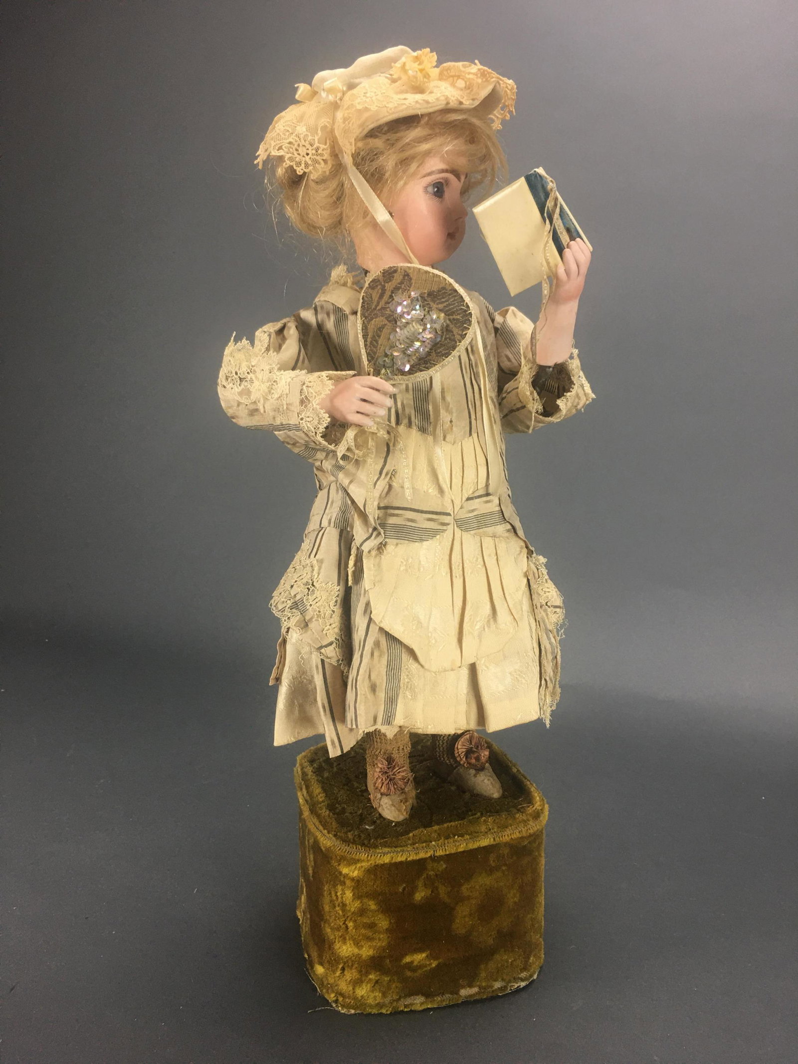 Automaton. Girl reading Fables. 19th c.: 19" (48 cm.) Standing upon a velvet-covered base is a bisque-headed doll with a blue glass paperweight inset eyes, dark eyeliner, lushly-painted lashes, rose-blushed eye shadow, brushstroked brows, ac