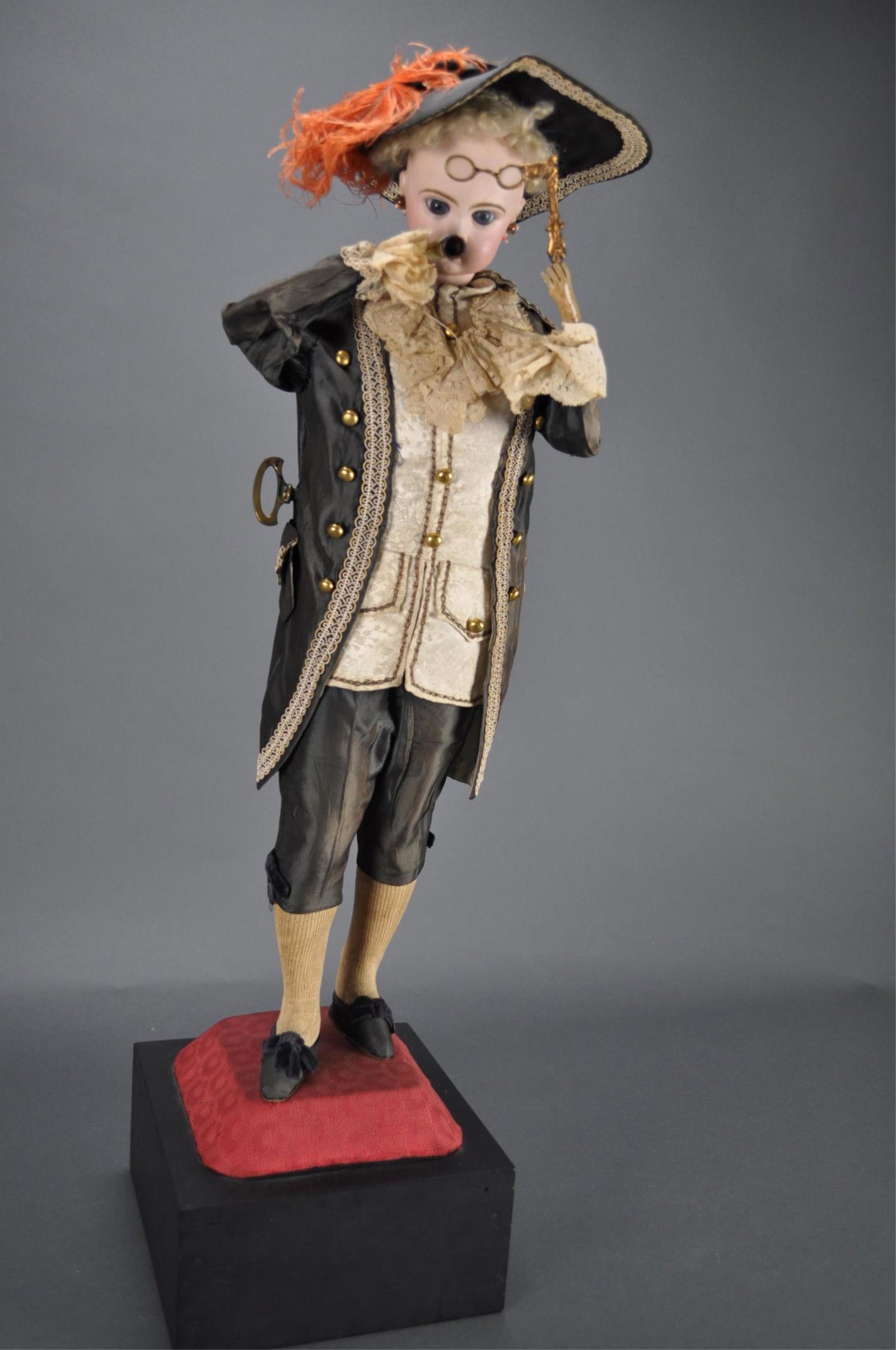 Automaton. The Marquis Smoker. Lambert.: 24" (61 cm.) Figure. 27" including wooden base. Standing upon a velvet covered platform is a bisque head gentleman doll with blue glass paperweight inset eyes, lushly-painted lashes and brows, accente