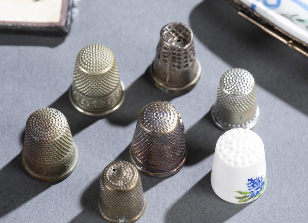 21 Sewing Implements.: Twenty-one sewing implements. ++ Six silver tone thimbles. ++ Ceramic thimble painted with flowers. ++ Fernware pin cushion. ++ McPherson tartan pin cushion. ++ Neuss Brothers pin card. ++ Unmarked st