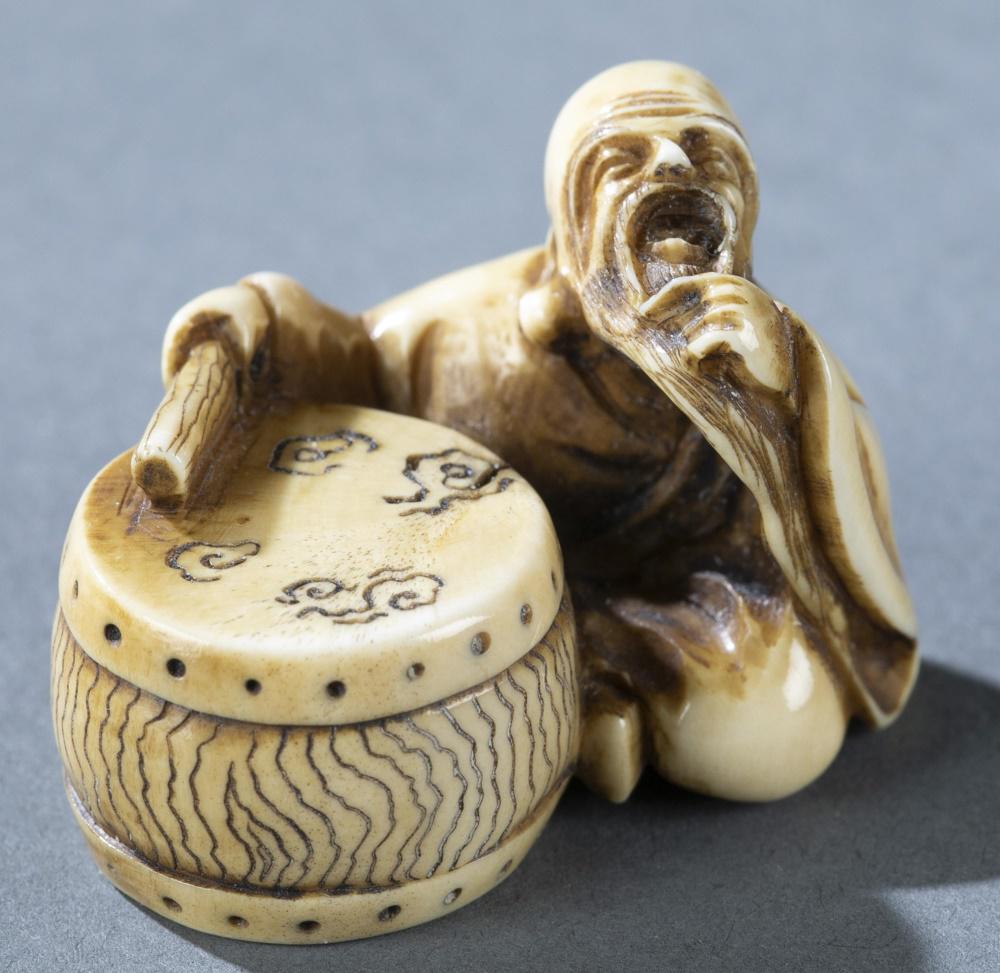 Netsuke of a seated man with drum, 19th c.: A marine netsuke of an old man seated next to a drum. Mid 19th century. Signed on underside of drum. H: 2.95cm. Condition: Wear to pattern consistent with age. Crack to hole on base. THIS LOT CONTAINS