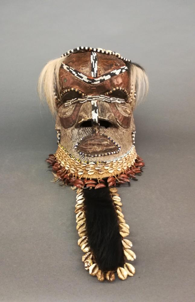 Kuba Style Helmet Mask. 20th c.: A Kuba style helmet mask. 20th century. Wood, shells, beads, pods, and hair. Central Africa. 11 1/2" x 10" x 25 1/2". Includes a stand.