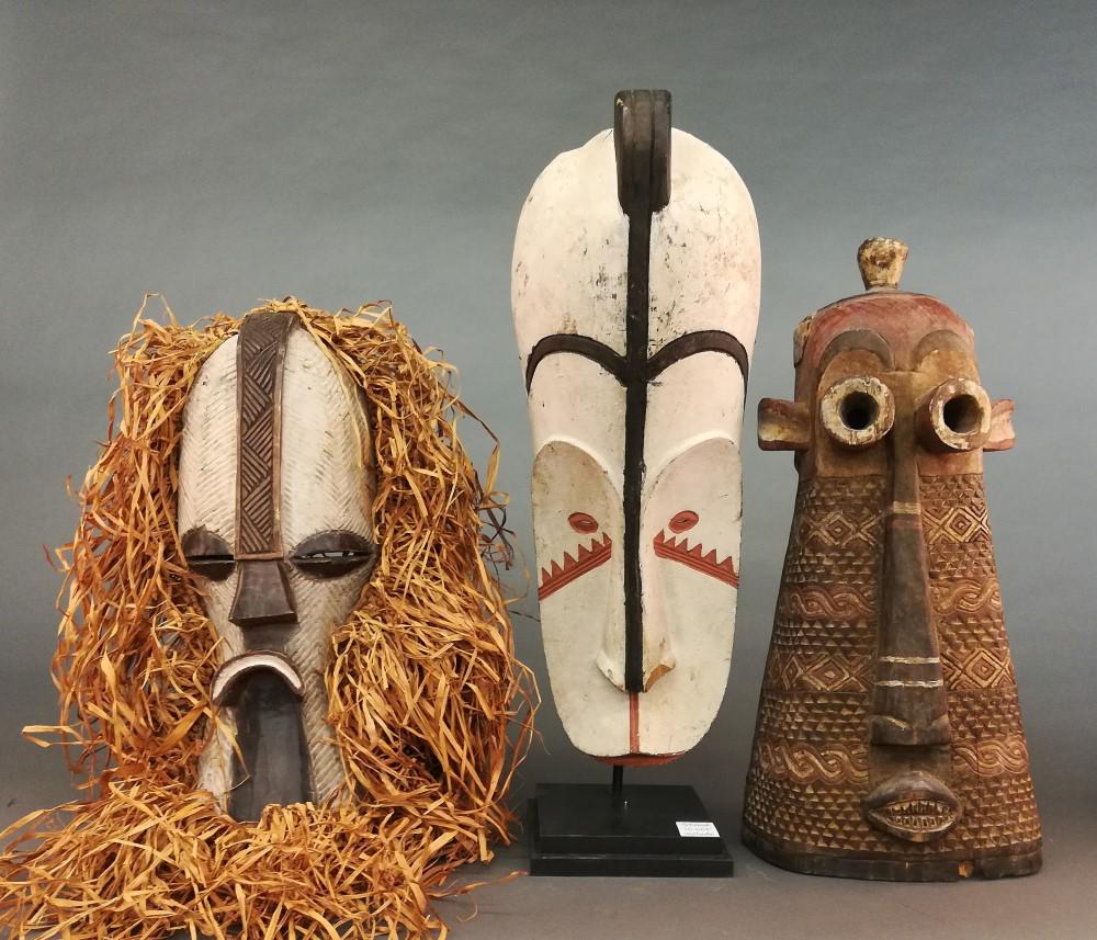 3 Central African Style Masks. 20th c.: A group of three Central African style masks. 20th century. Wood. Each mask is approx. 25 1/2" x 17" x 6". Chipping and cracks present throughout. Mask on the far right includes a stand.