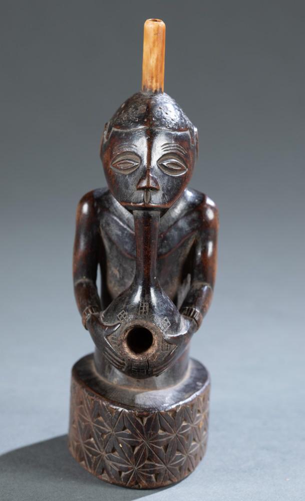 Kongo Style Figure w/ Pipe, 20th c.: A Kongo style figure with pipe. Central Africa. 20th century. Wood and possibly bone. 6 3/4" x 2 1/4" x 3". Condition: some wear throughout. Provenance: Private New York Collection.