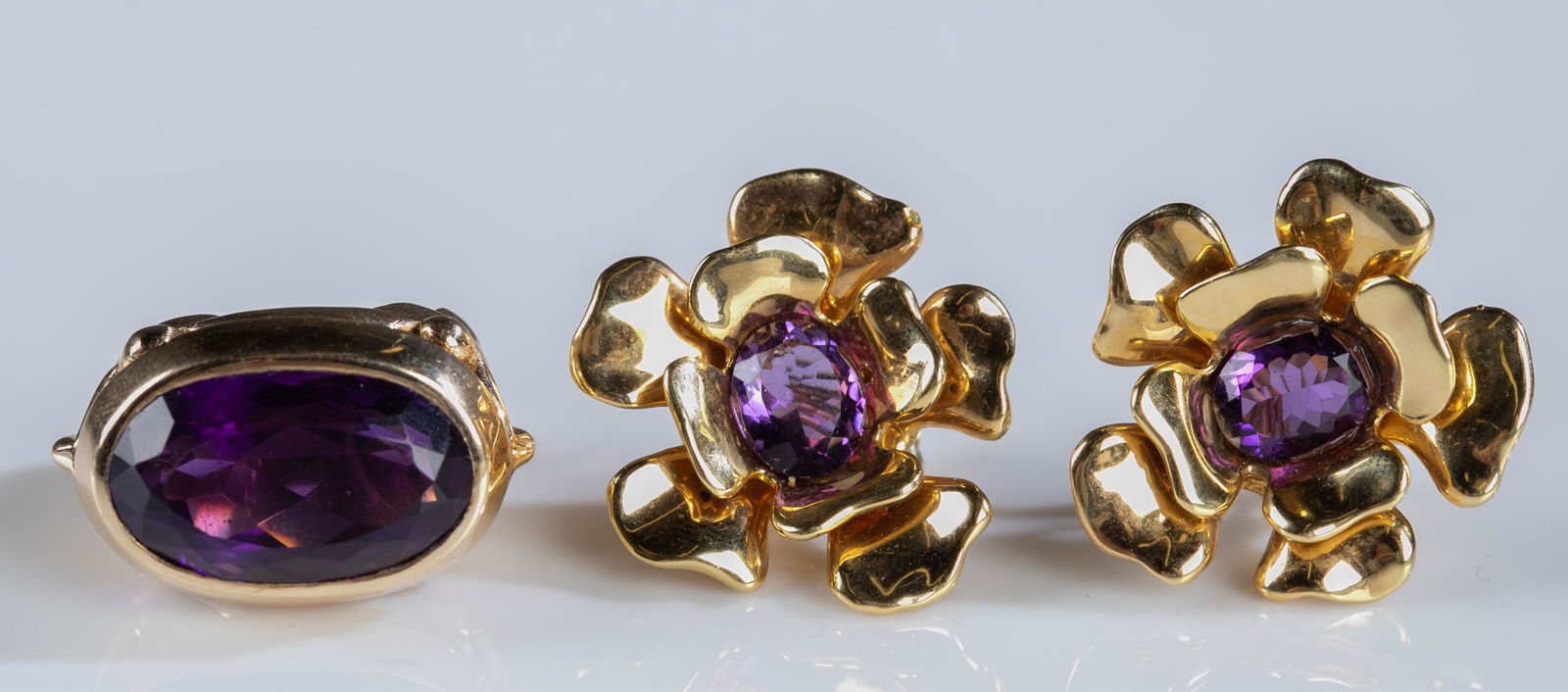 Pair of 14k gold amethyst earrings and ring.: A pair of 14k yellow gold amethyst earrings and ring. ++Ring with oval cut amethyst. Stamped "14k C.I." inside band. Size 5. Approximately 15.6g. ++ Floral form clip on earrings with central oval cut