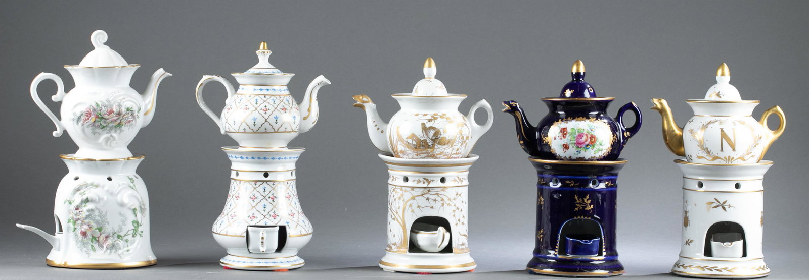 5 Sets of porcelain tea pots and warmers: A group of five sets of porcelain tea pots and warmers. Marked on base. Largest: 10 1/2" x 6 3/4" x 4 1/2". Smallest: 9 1/2" x 6 1/2" x 4 1/2". ++ Cobalt blue with gold and floral design. Tape residue