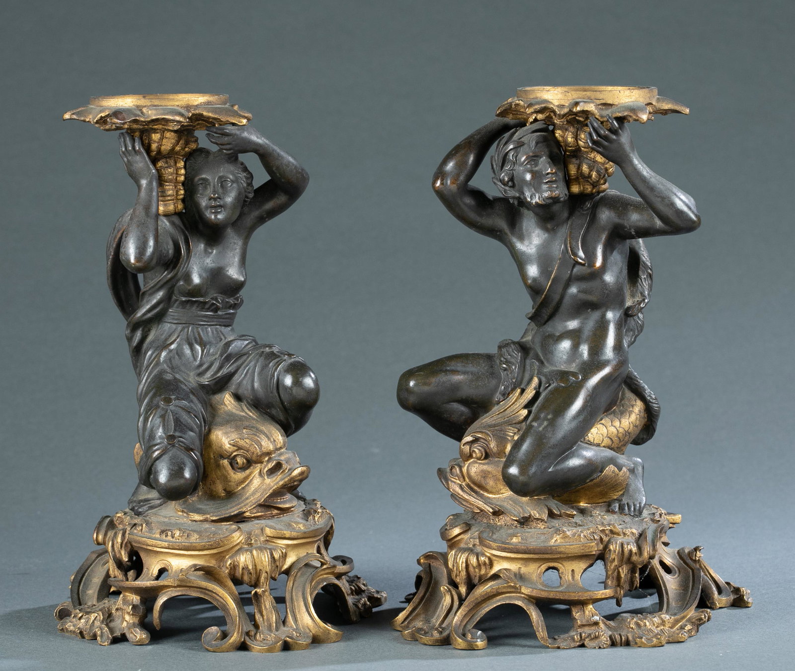 Pair of Bronze figural candle holders, 19th c.: A pair of Rococo Revival bronze figural candle holders, 19th century. Depicting a Classical male figure with laurels perched on a dolphin. 9 3/4" x 6 3/4" x 6". Shipping: This lot does not qualify for