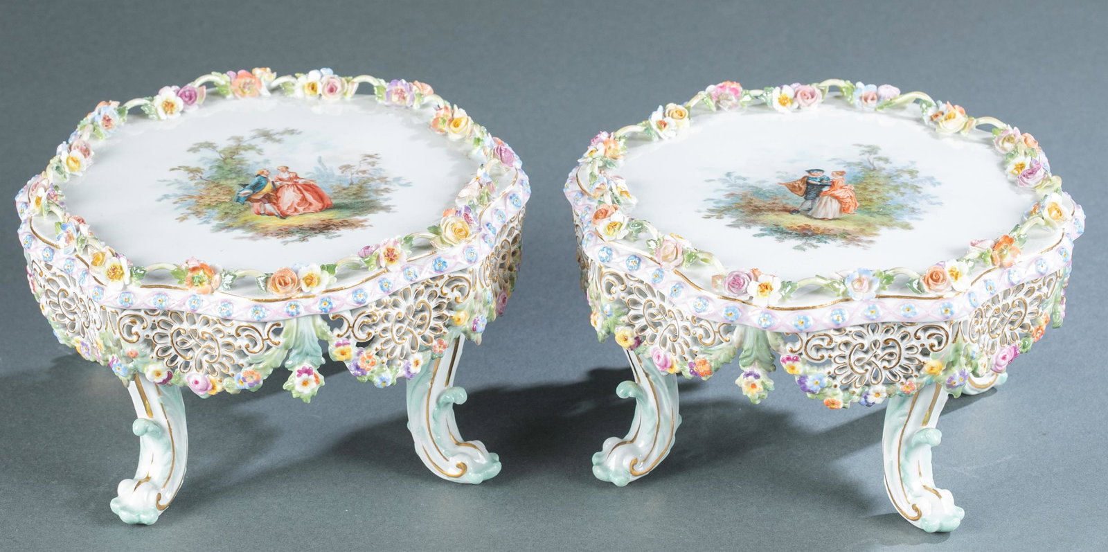 2 Meissen plateaus with sprigged flowers.: A pair of Meissen porcelain plateaus with sprigged flowers and painted central design of two figures in a garden, circa 1815-1924. Round scalloped form on 4 legs with pierced skirt. Marked with blue c