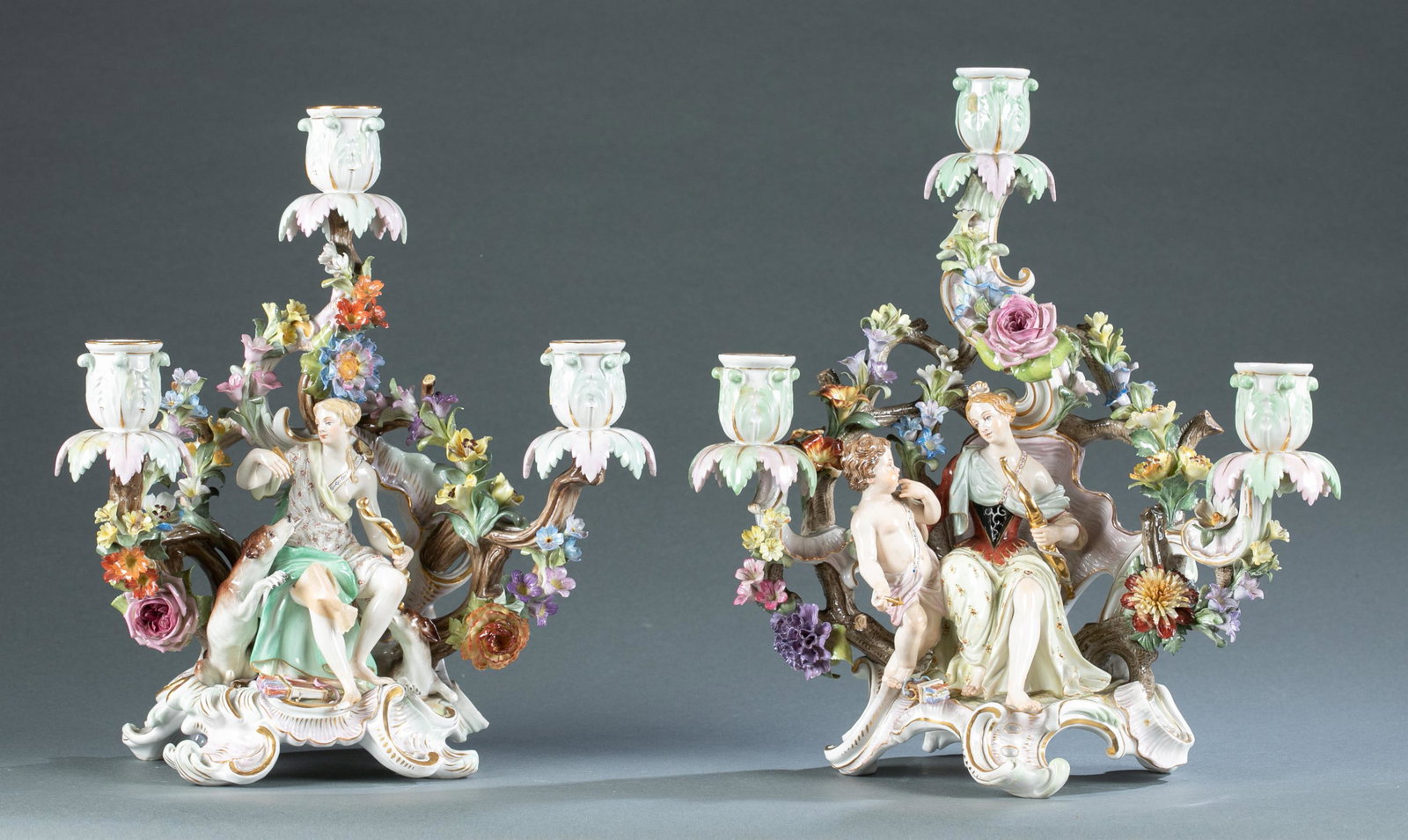 Pair of Meissen Style figural 3-light candlesticks: A pair of Meissen style porcelain figural three light candlesticks, circa 1815-1924. Figure of seated Artemis with hound, and Venus with cupid. Faintly marked on base with blue crossed swords under gl