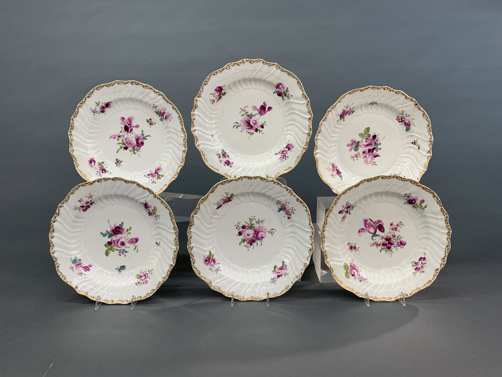 6 Meissen porcelain plates, 19th c.: A group of six Meissen porcelain plates with purple flowers and gold rim. Circa 1815-1924. Marked on base with blue crossed swords under glaze. 9 1/2" x 9 1/4" x 1 1/4". Condition: Discoloration and s