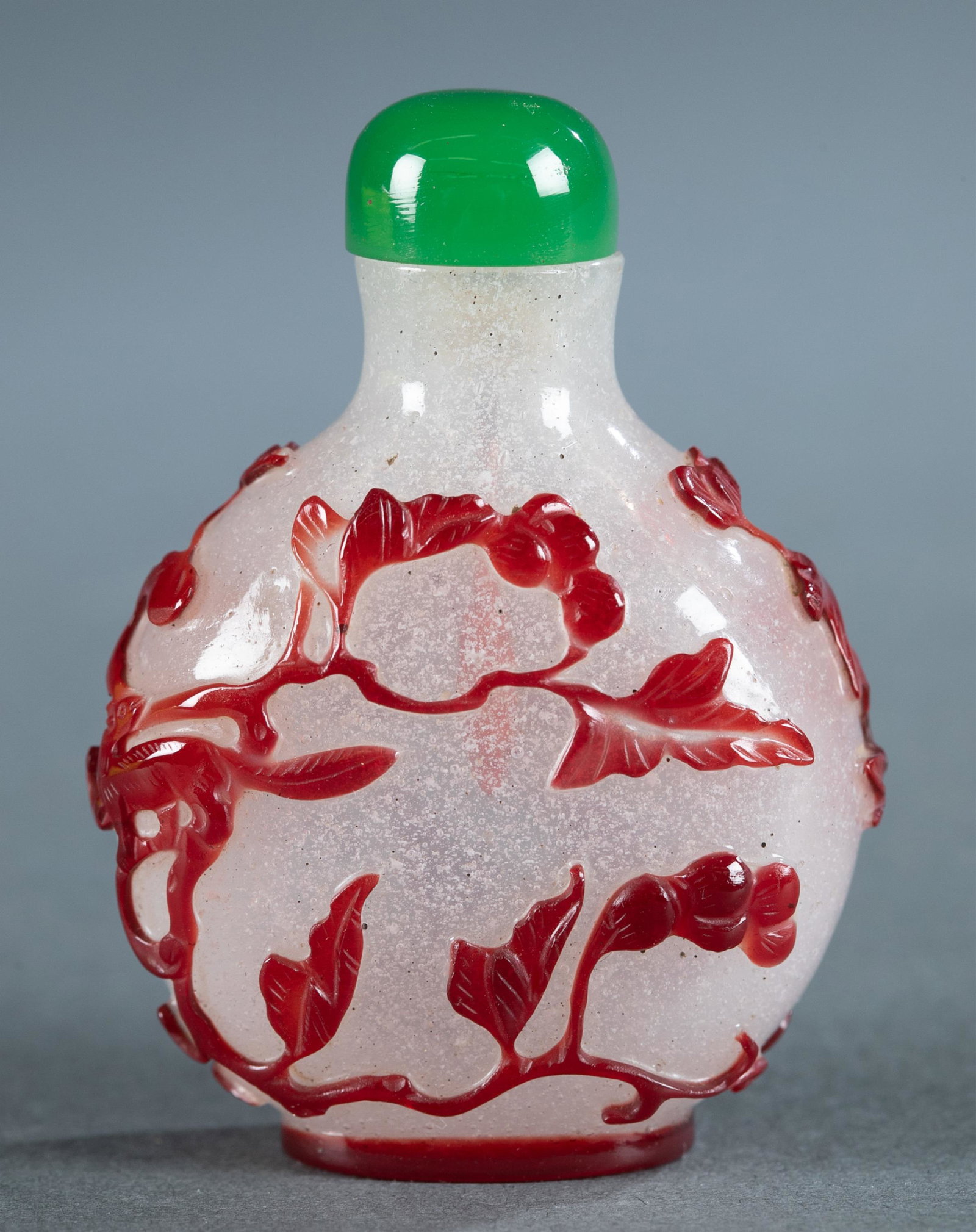 Peking glass overlay snuff bottle, 19th c.: A red over snowflake Peking glass snuff bottle, 19th century. Flattened round form red glass depicting a squirrel in a tree. Having a green glass stopper. 2 5/8". Provenance: Sotheby's tag.