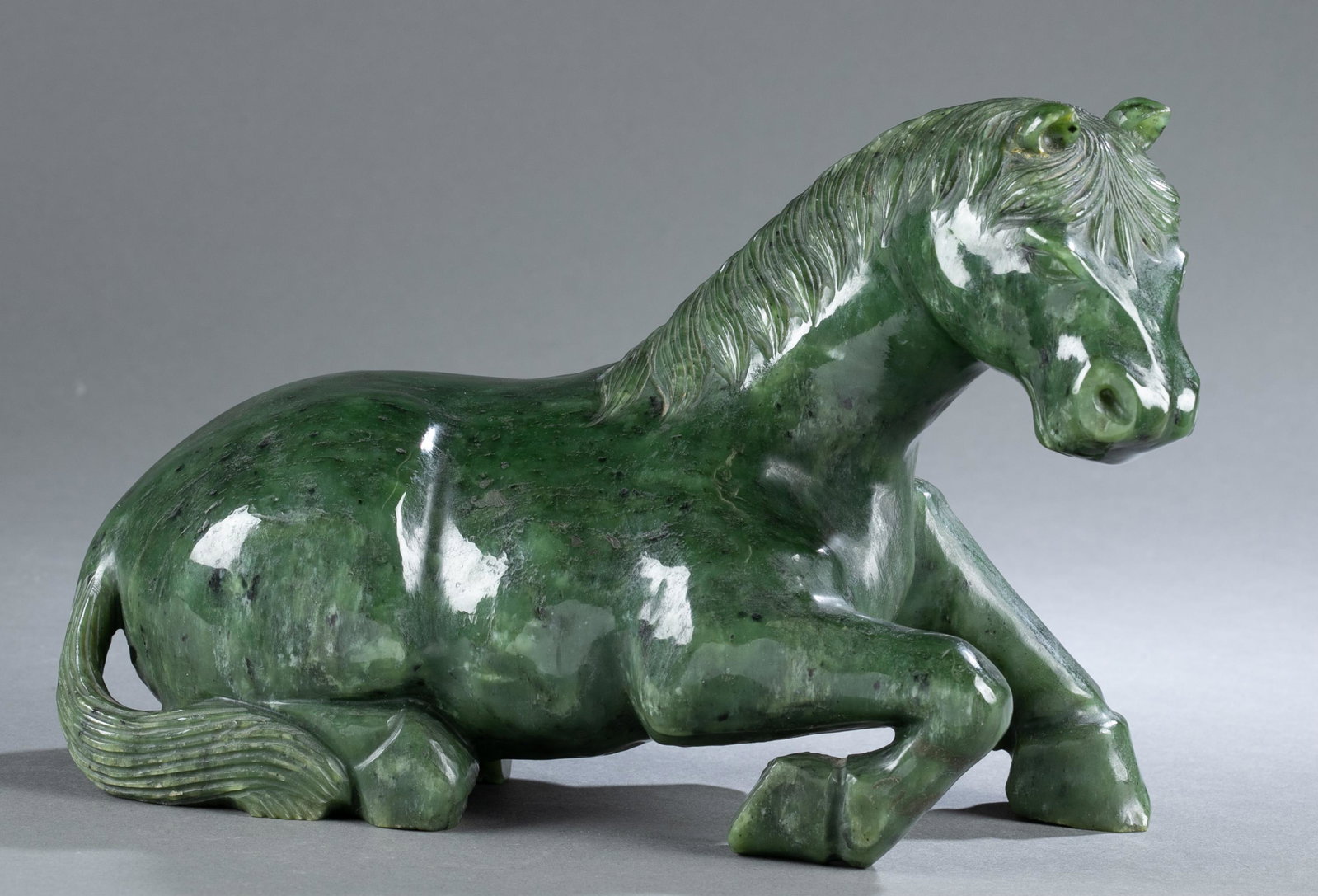 Chinese jade sculpture of a reclining horse.: A Chinese jade sculpture of a reclining horse. 20th century. Spinach jade horse depicted lying with legs folded underneath. 7" x 11" x 3 3/4". Condition: Light wear to surface. Provenance: From the es