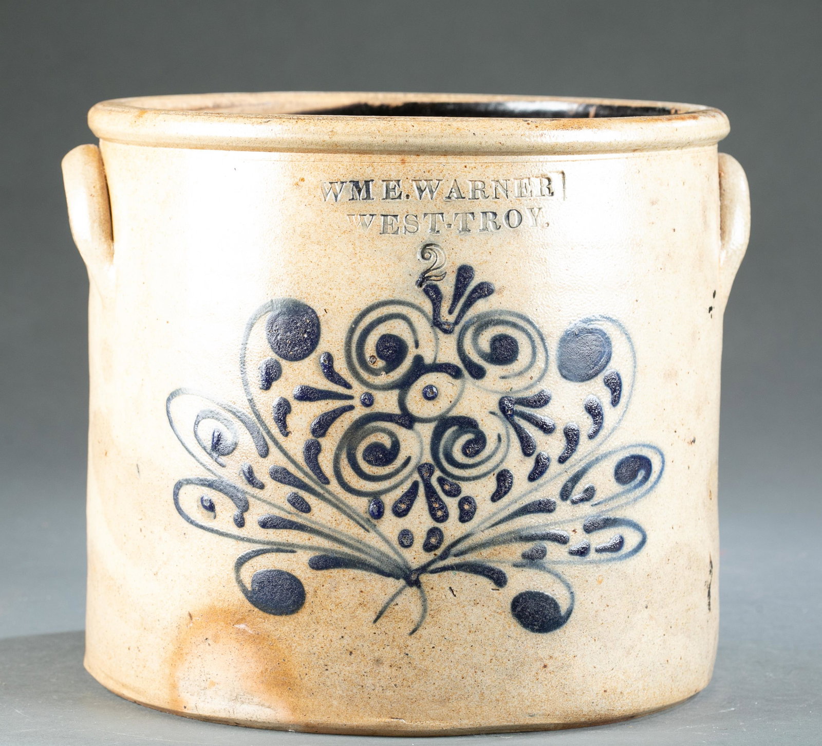 William E. Warner West Troy stoneware crock.: A William E. Warner, West Troy, NY. stoneware crock with blue slip swirl decoration and wooden lid and scoop. Straight sided crock with rounded rim and applied lug handles. 19th century. Marked "WME. 