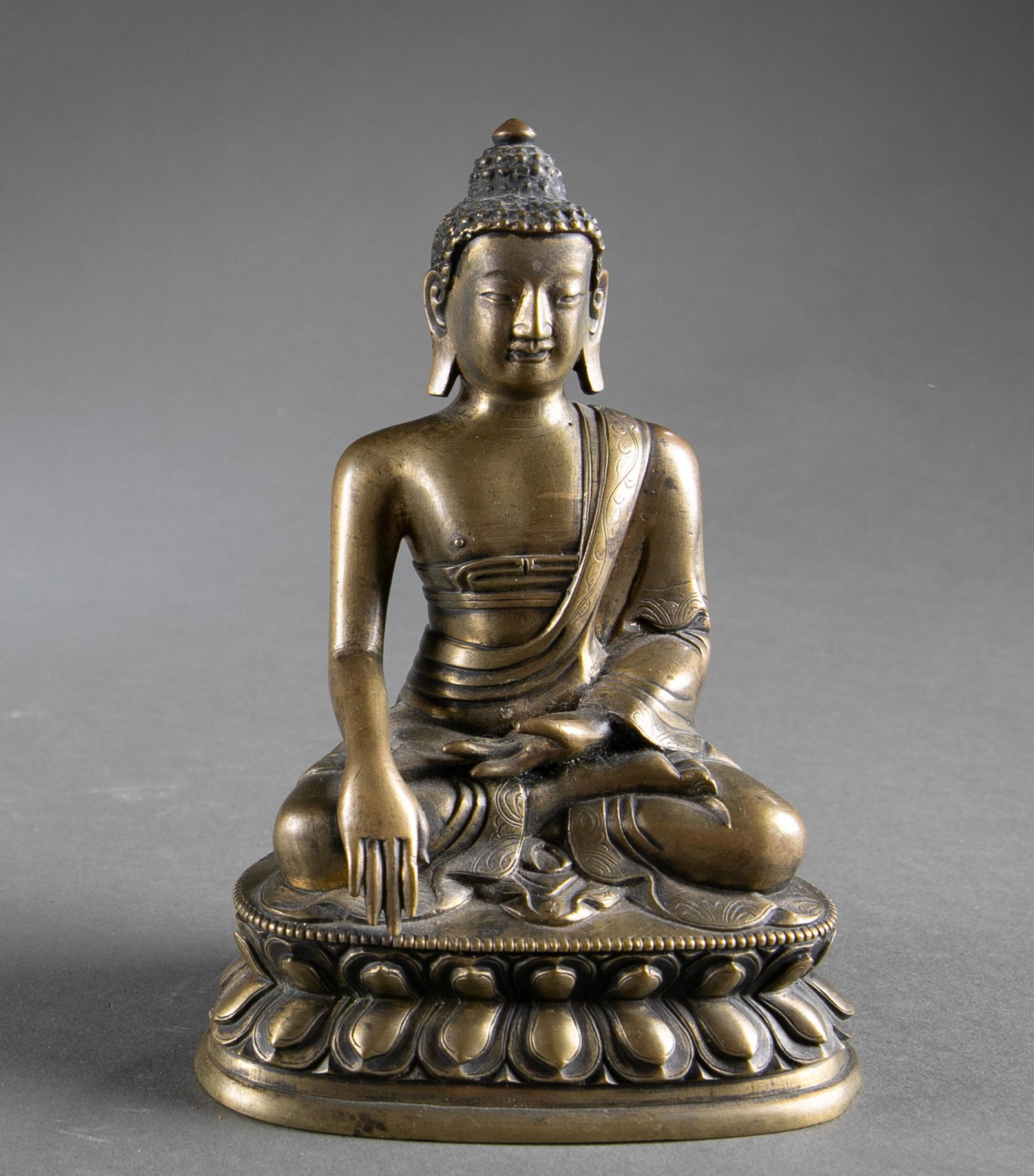 Bronze figure of sitting Buddha.: A bronze figure of sitting Buddha on a lotus base, both legs crossed. 6 1/2" x 4 7/16". Condition: Some multiplier missing from his left hand. Some abrasion and scratches to the body.