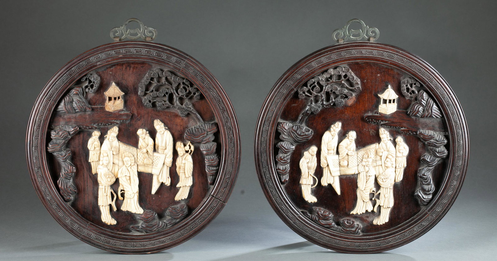 Pair of Chinese wooden plaques with bone carvings: A pair of Chinese wooden plaques with bone carvings. The wooden plaques are a full round shape decorated with pine tree and stone carvings. The bone carvings depicts a group of people in a garden. 16"