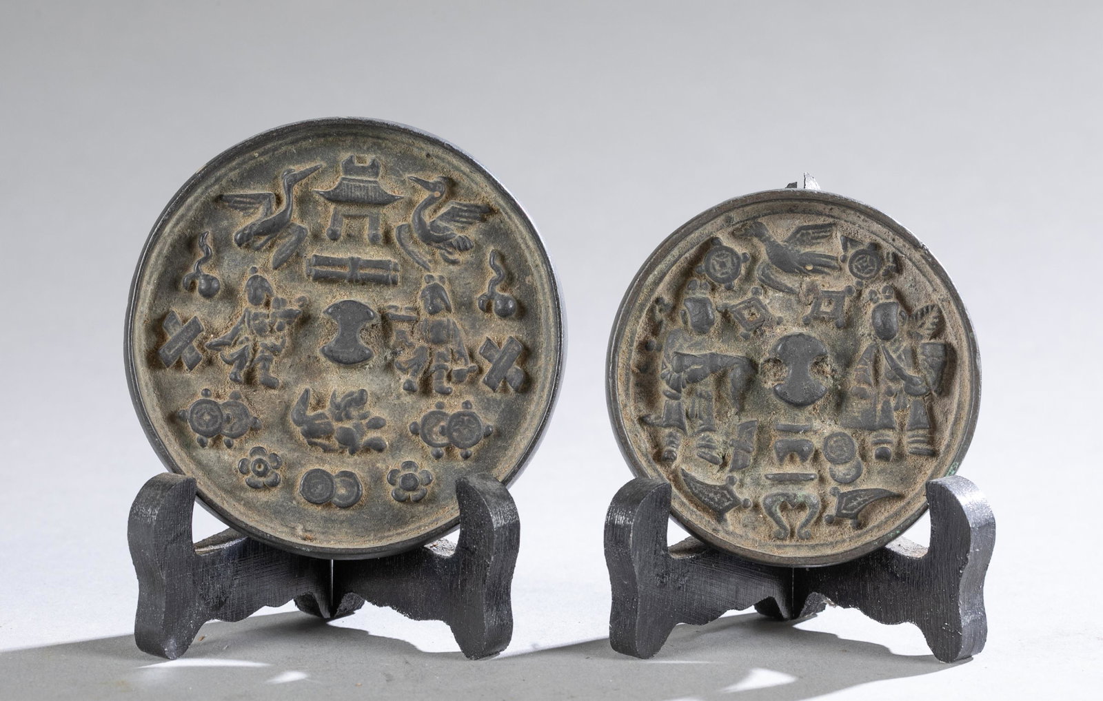 Pair of Chinese bronze mirrors, 19th century.: A pair of Chinese bronze mirrors, 19th century. Raised design of traditional Chinese motifs and implements on the back. Includes with wood stands. 3 3/4" diam.Condition: Age-related and using abrasion