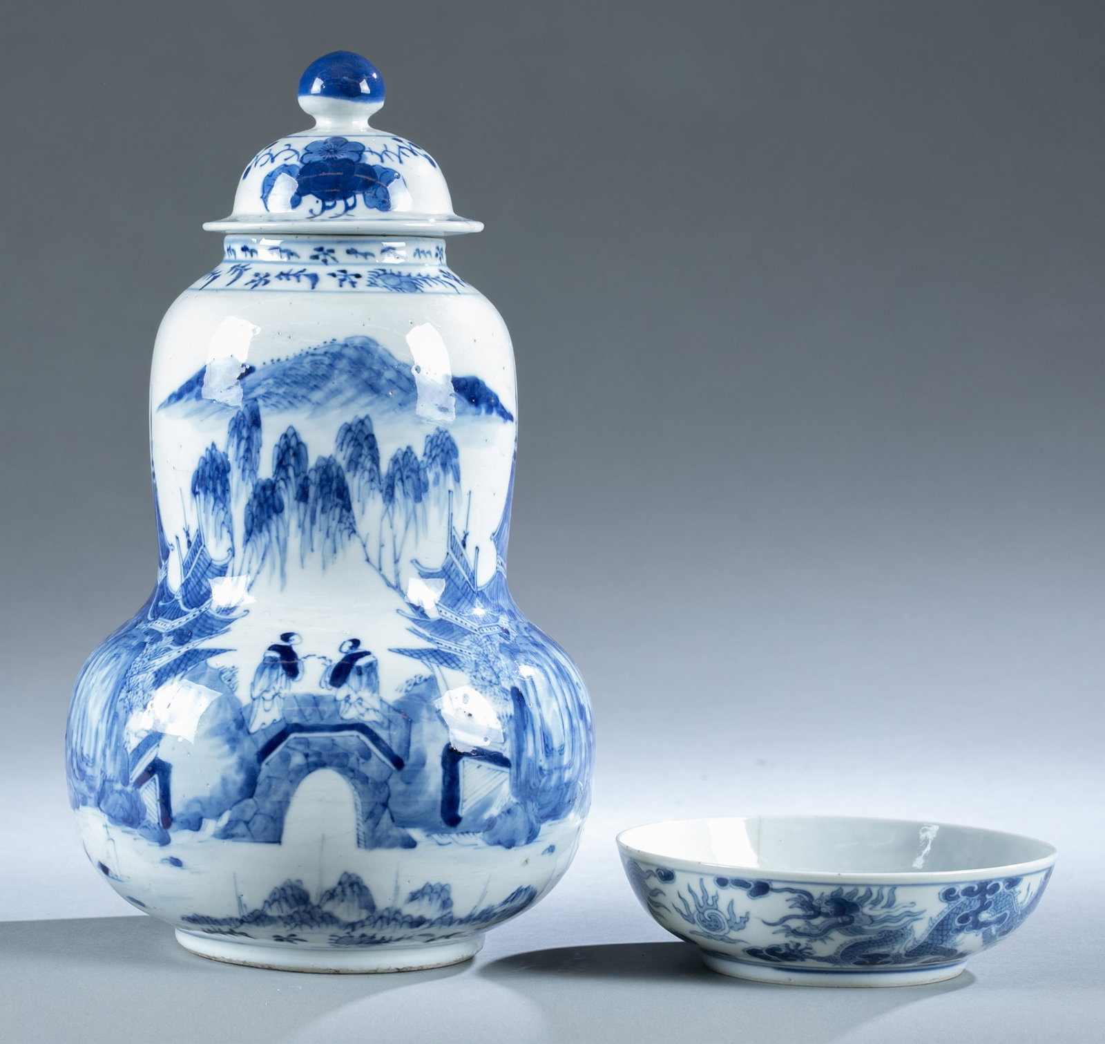 2 Blue and white porcelain containers.: A group of two blue and white porcelain containers. Including a Chinese gourd-shape lidded jar, possibly of the Republic period, depicting landscape scene. "Kangxi Nianzhi" mark to the bottom. 11 1/2"