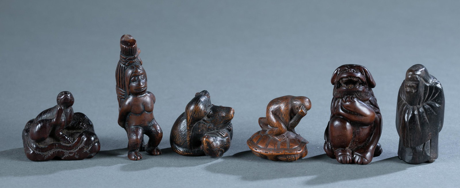 Group of 6 Japanese wooden netsuke.: Group of 6 Japanese wooden netsuke. Including a three-rat carving. 1" x 1/8". A crossed-arm old man. 2" x 1". A monkey on the top of turtle shell. 1 1/4" x 1 1/8". A scratching cat on the ground. 1 3/