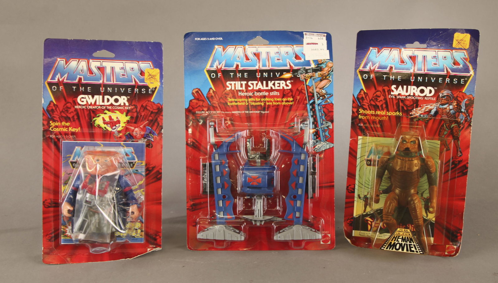 3 MOTU action figures MOC.: A group of three Mattel Masters of the Universe action figures. Mint on Card ++ MOTU He-Man Movie 1987 Saurod 5.5" figure action figure on card. 11 1/2" x 6" x 1 3/4" ++ MOTU He-Man Movie 1986 Gwildor