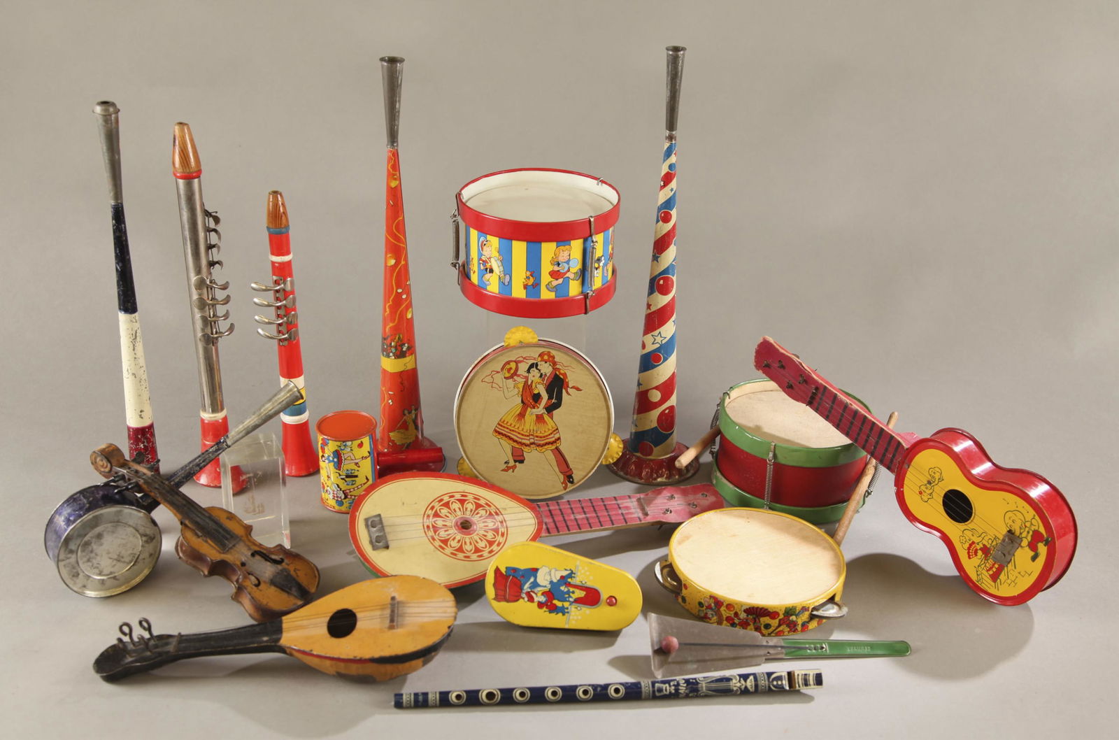 18 Vintage noisemakers and instruments.: A group of eighteen vintage tin lithograph and wood noisemakers and instruments. Including tin litho flutes, two drums, and four stringed instruments. Largest 14 1/2" x 2" x 5 1/4" and smallest 5" x 3