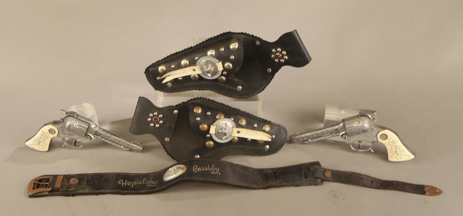 Wyandotte Hopalong Cassidy cap gun set.: Wyandotte Hopalong Cassidy cap gun set. Two die cast cap guns with faux ivory grips, one pistol missing one grip. 30" leather belt with two holsters. Revolvers 8 1/2" long. Condition: Both pistols fun