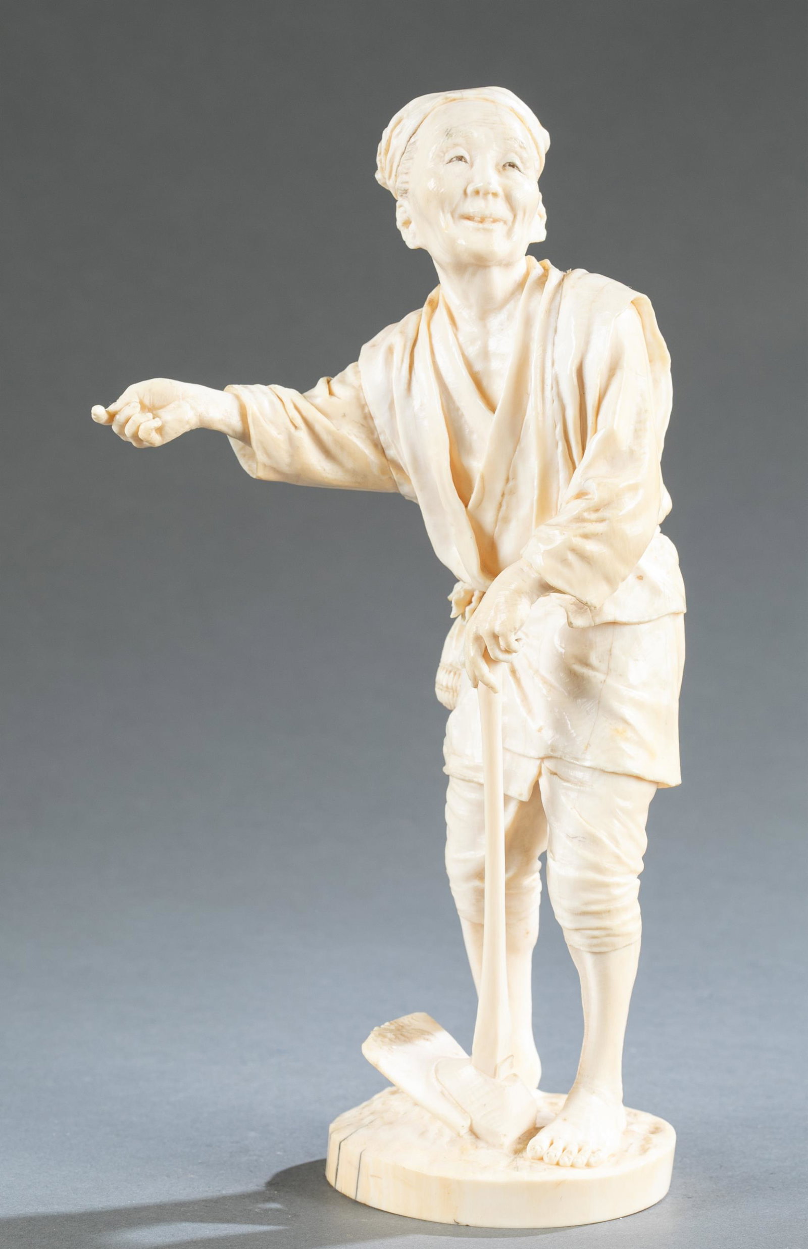 Ivory Okimono of a farmer, 20th century.: A carved ivory okimono of a farmer. Standing on circular base holding a hoe. Signed on base. 10 1/4" x 5" x 3". NOTE: VIRGINIA BUYER ONLY. THIS LOT CONTAINS ANIMAL OR PLANT MATERIAL THAT MAY BE RESTRI