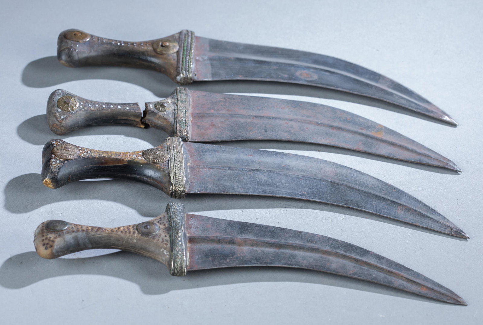 4 Yemeni Jambiya daggers.: A group of four Yemeni Jambiya or Djambia daggers with horn handles. All feature riveted bone handles, chased silver band around cross guard, and bronze medallions. One dagger has break through handle