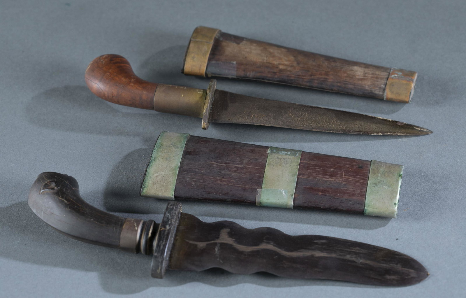 2 Philippine Moro punal daggers.: A group of two Philippine Moro punal or gunong daggers. ++ Dagger with burl wood handle and sheath. Copper cross guard and fixtures. 5 1/2" straight double edged blade. 9" overall and 6" sheath. ++ Pu