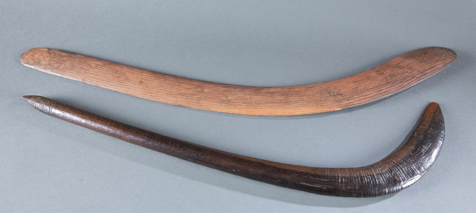 2 Australian Aboriginal weapons.: A group of two Australian Aboriginal weapons, 20th Century. ++ Wood boomerang. 29 1/2' long. ++ Wood waddy, nulla-nulla or boondi warclub. Straight shaft with flared and bent head. Carved decoration a