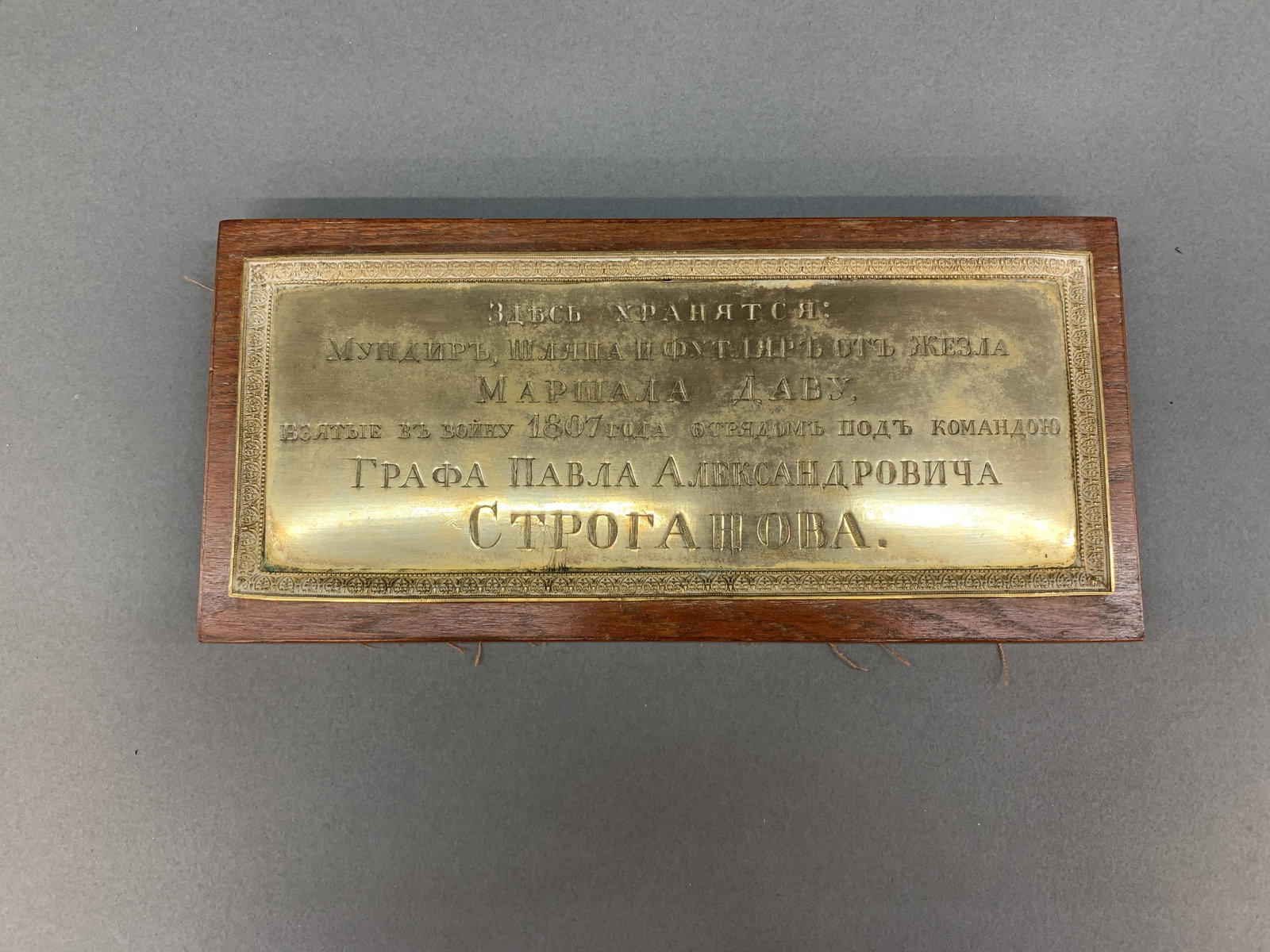 Russian plague for Field Marshal Davout's uniform.: Imperial Russian display plague for Napoleonic France Field Marshal Davout's uniform. Embossed brass plate with floral border mounted to wood backing. In Cyrilic the plaque reads: "HERE ARE THE HOLDIN